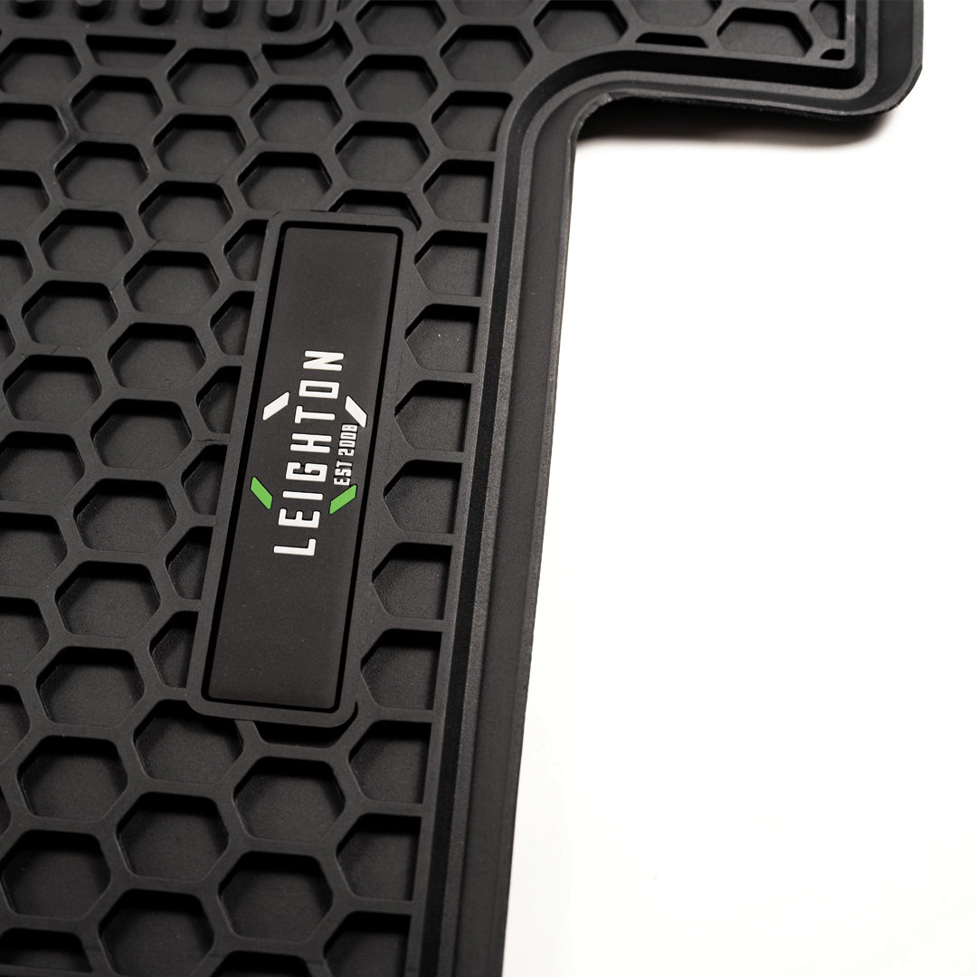 Close-up of a black rubber car mat featuring a honeycomb texture and a logo that reads "LEIGHTON EST 2009."