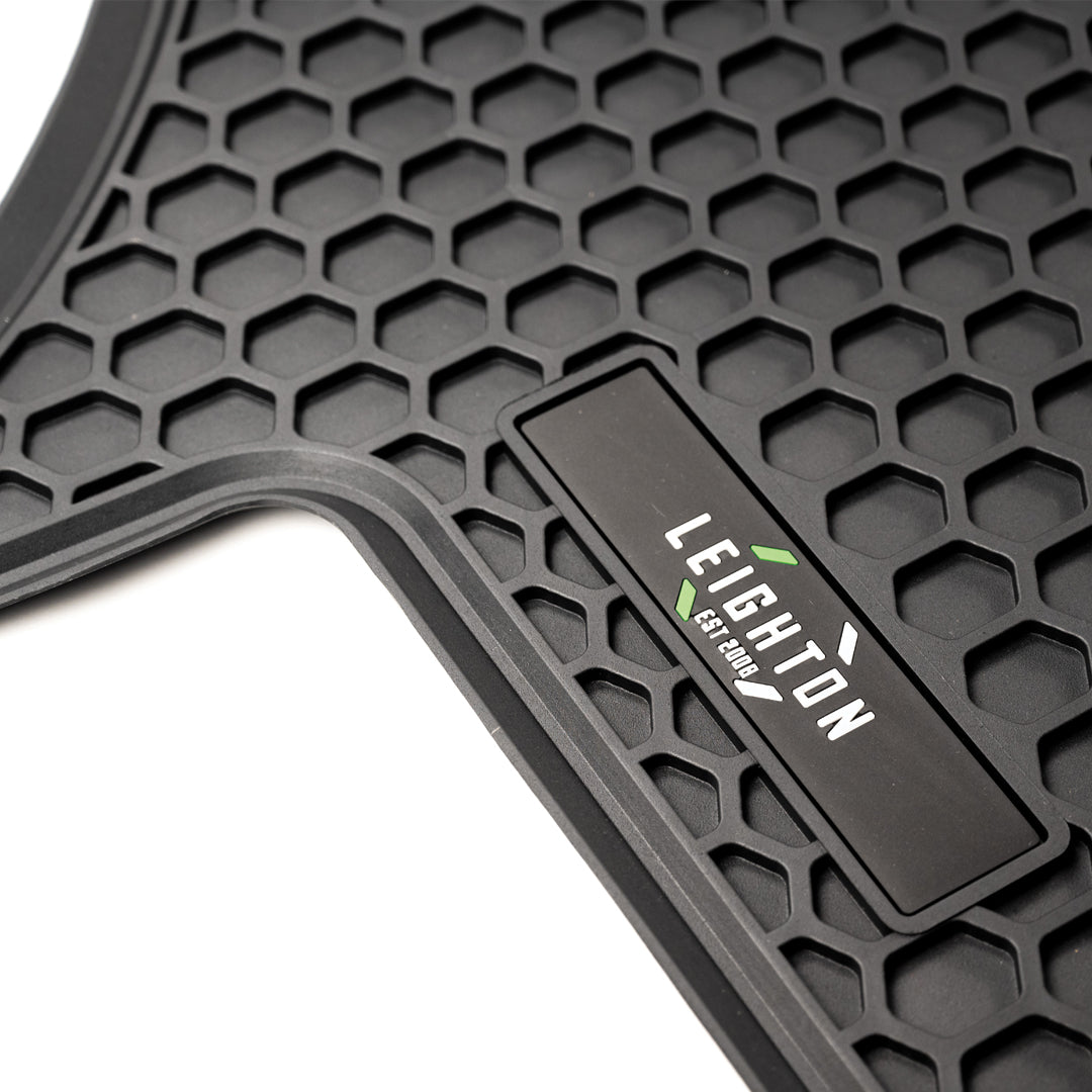 Close-up of a black rubber floor mat featuring a honeycomb pattern and a tag that reads "LEIGHTON EST 2004."