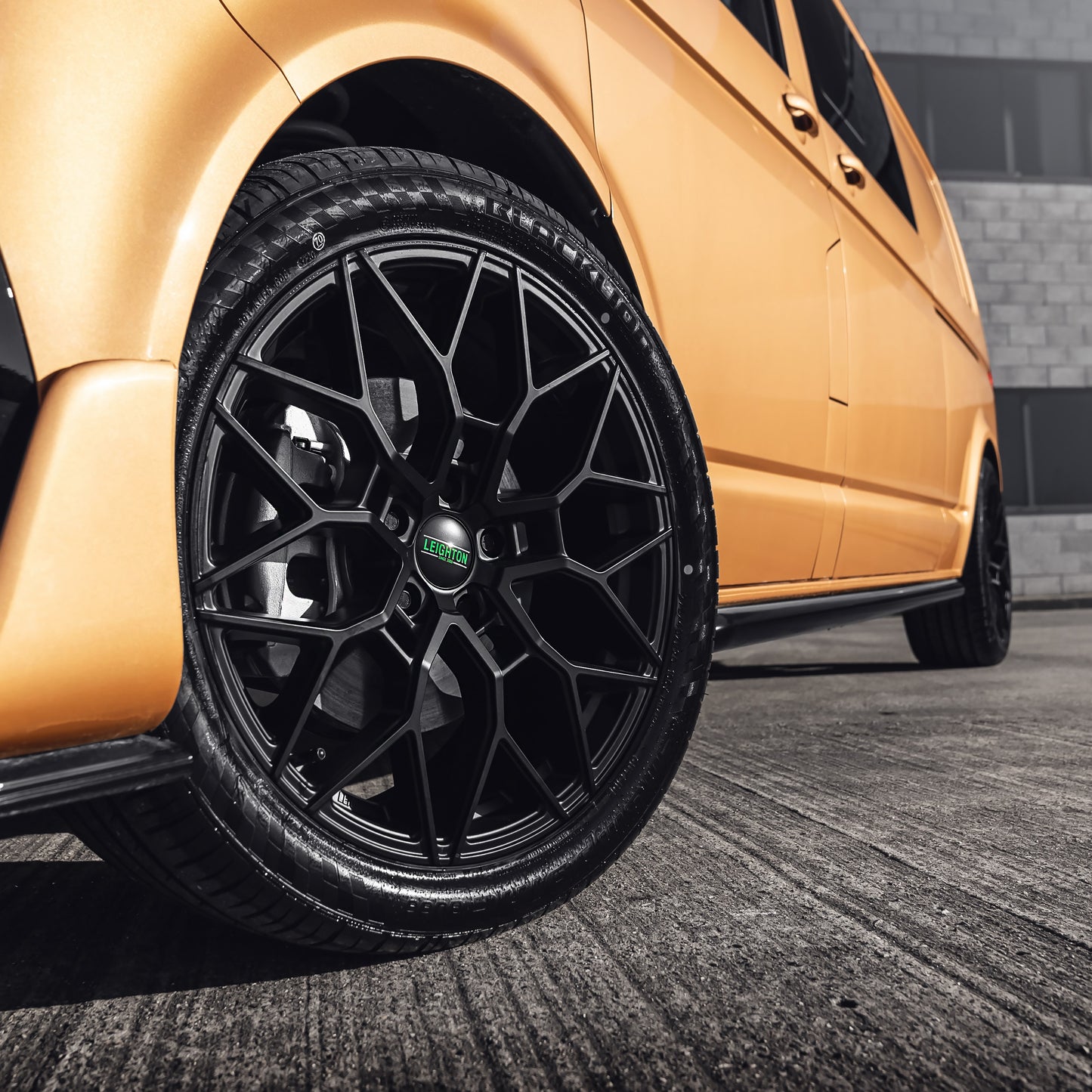 A close-up of a stylish black alloy wheel on a sleek orange vehicle, highlighting its unique design and glossy finish.
