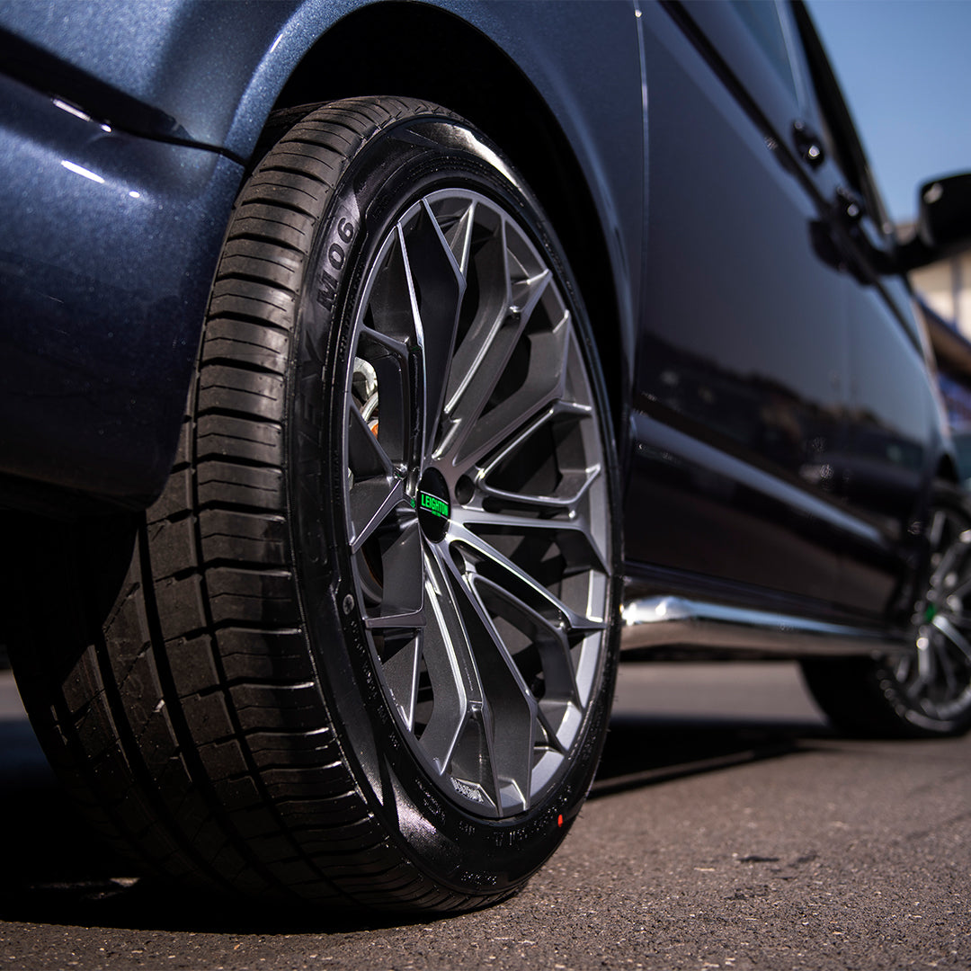 Close-up of a stylish car wheel with a modern alloy rim and low-profile tire, parked on a sunlit street.