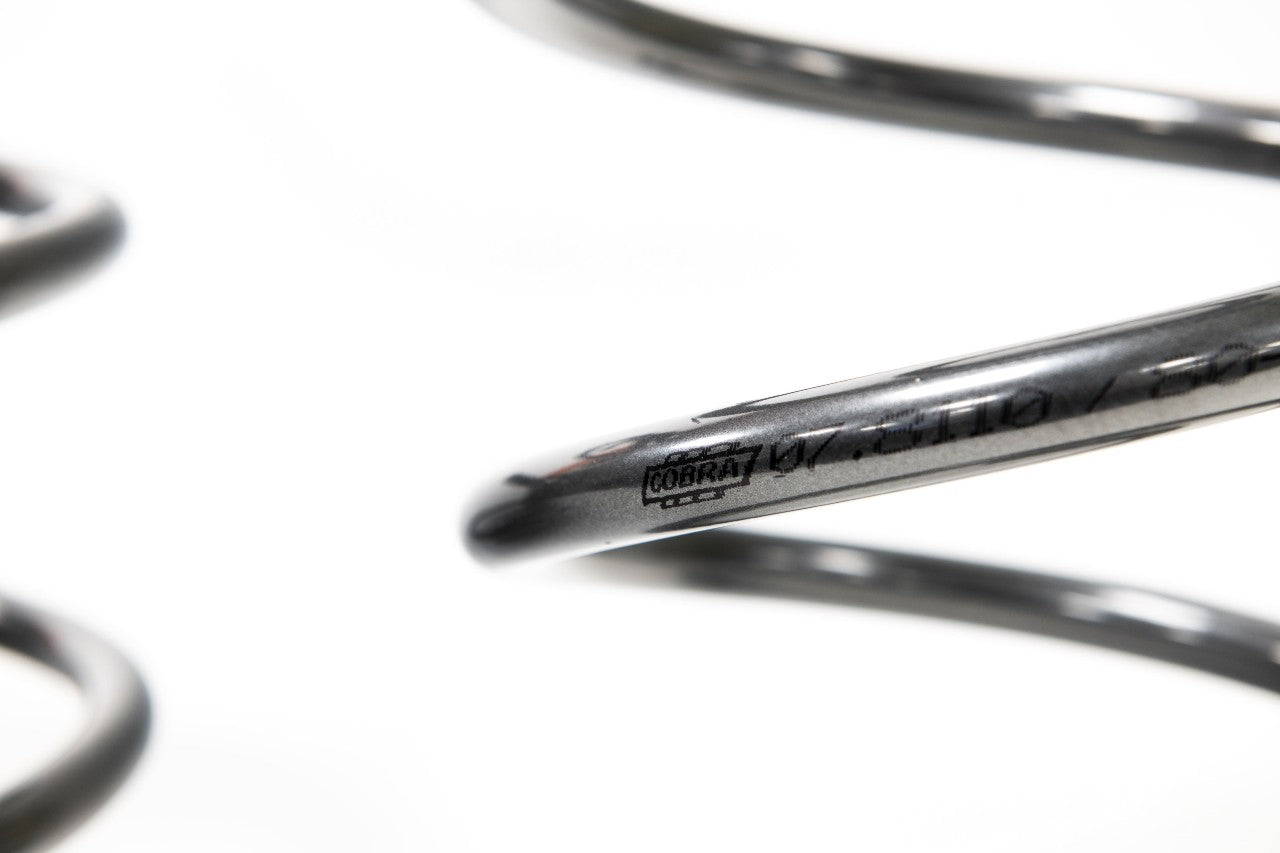 Close-up of a sleek metal coil spring, featuring the engraved "COBRA" logo and identification numbers on its surface.