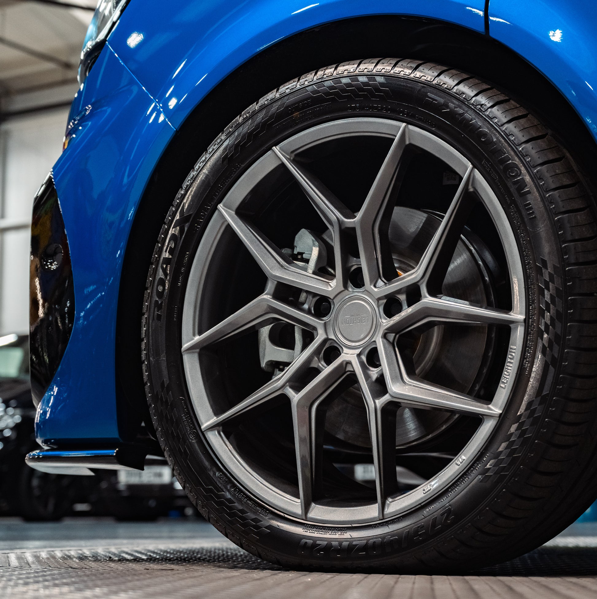 Close-up of a stylish silver alloy wheel on a blue car, showcasing intricate spokes and a high-performance tire.