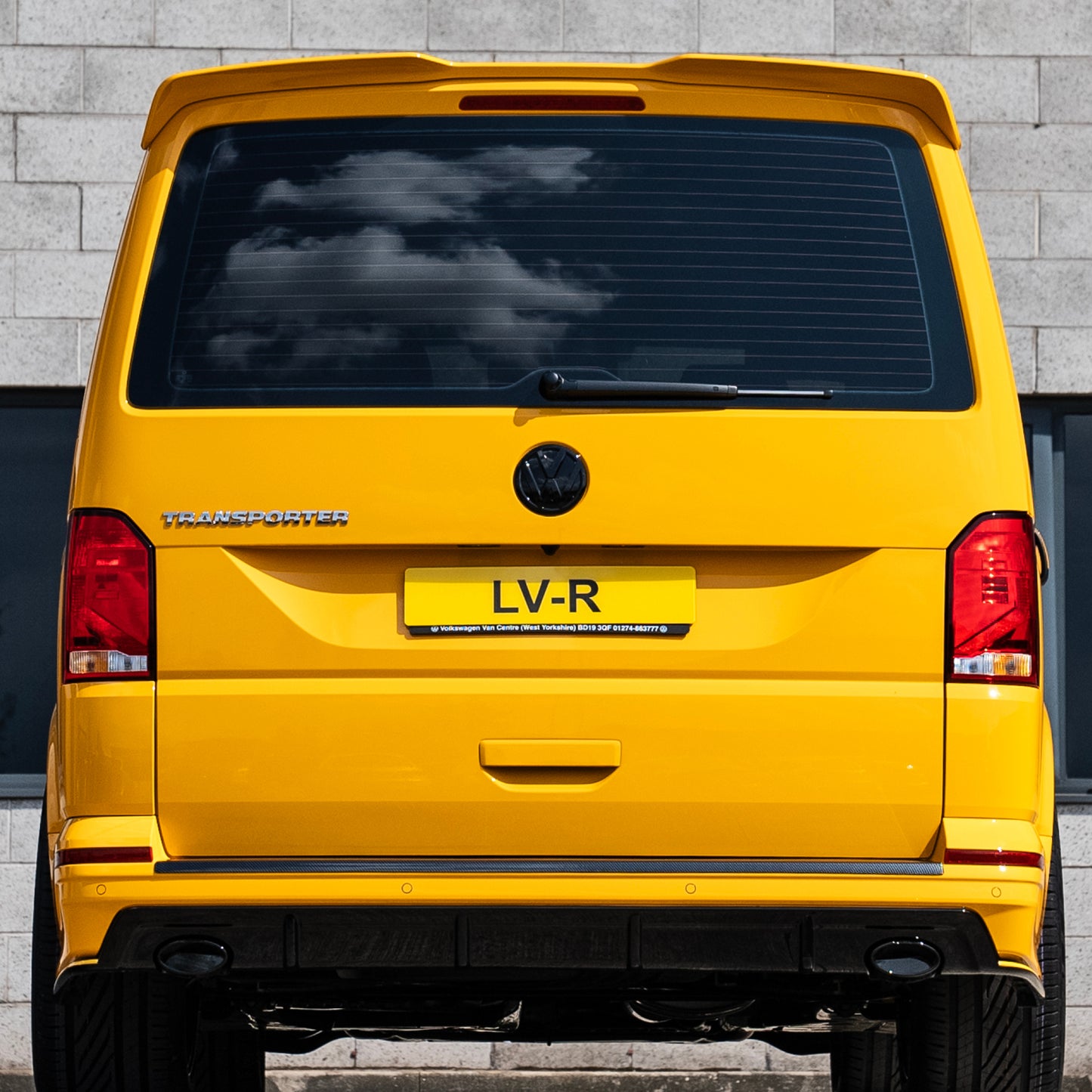 A vibrant yellow Volkswagen Transporter viewed from the rear, featuring a sleek design and a personalized license plate "LV-R."