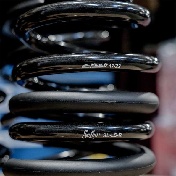 Close-up of two black coil springs, featuring brand markings "Eibach 47/22" and "Solow SL-LS-R," against a blurred background.
